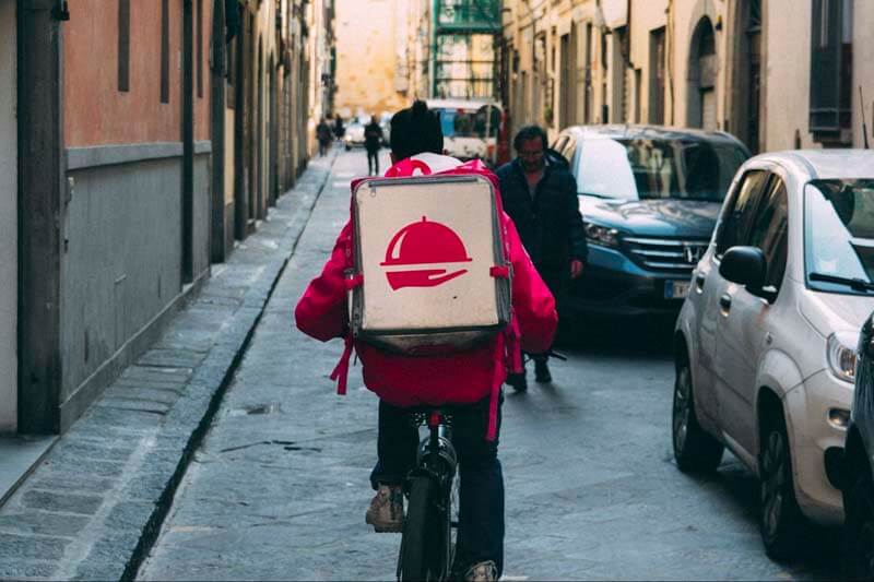 A food delivery worker delivering food on a bicycle through a busy city street