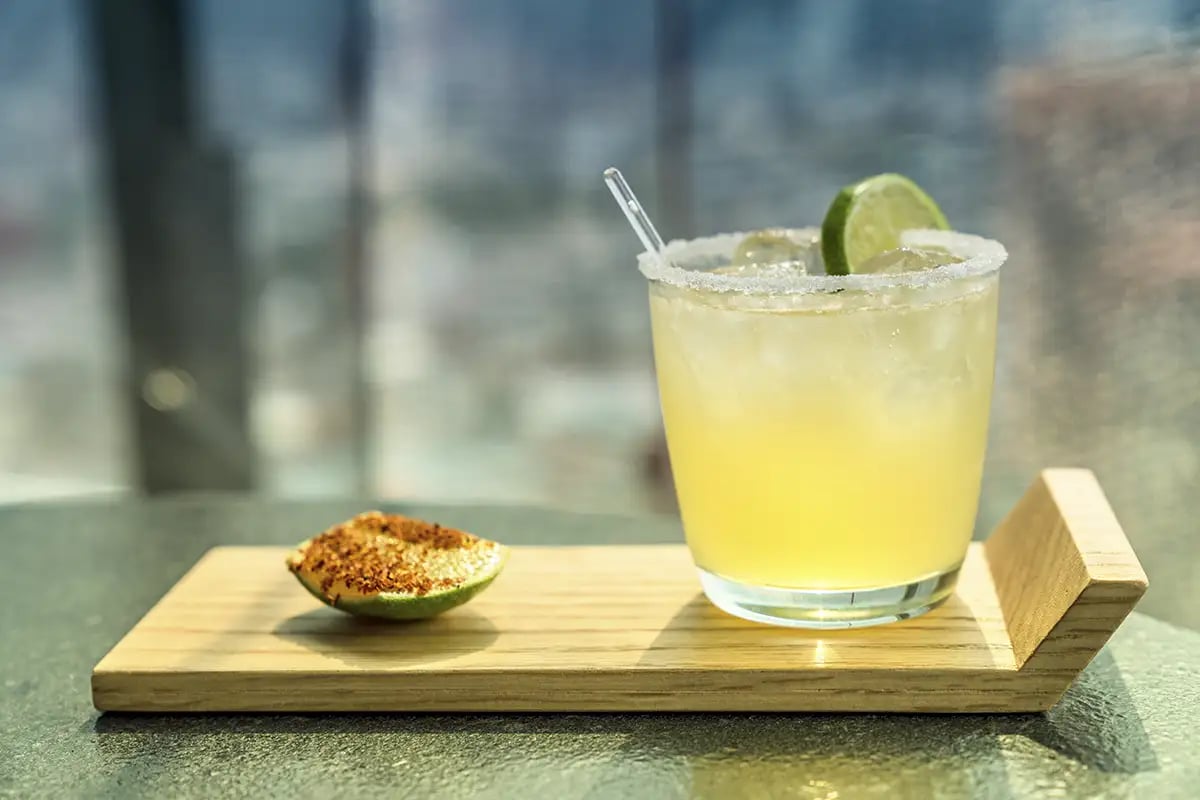 A margarita made with sotol and a lime garnish served on a wooden serving board
