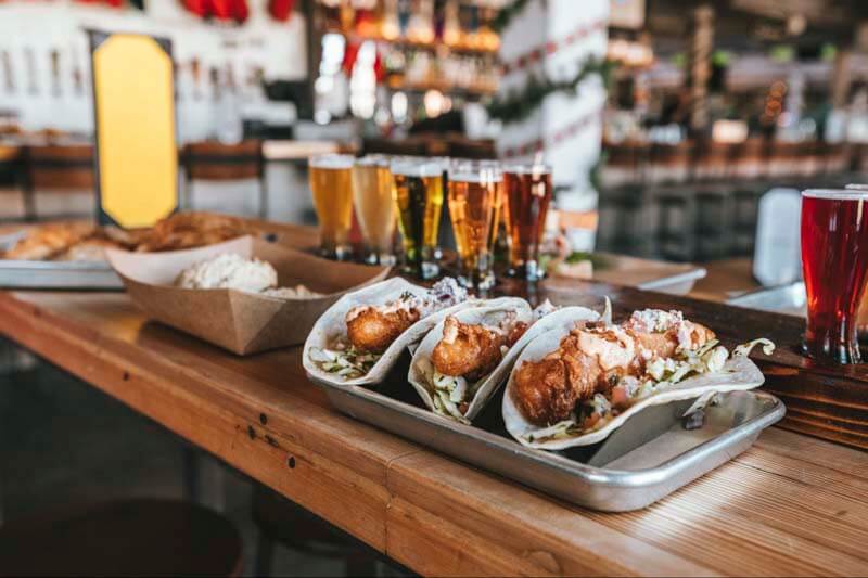 A soft taco platter served with various sides and a flight of beer at a bar