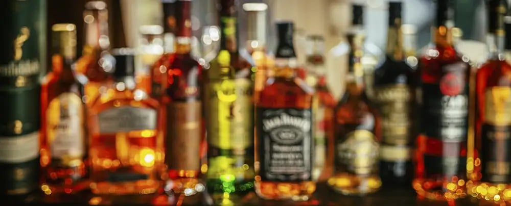 A variety of whiskey bottles on a shelf behind a bar
