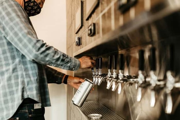 Bartender pouring beer from tap into a crowler