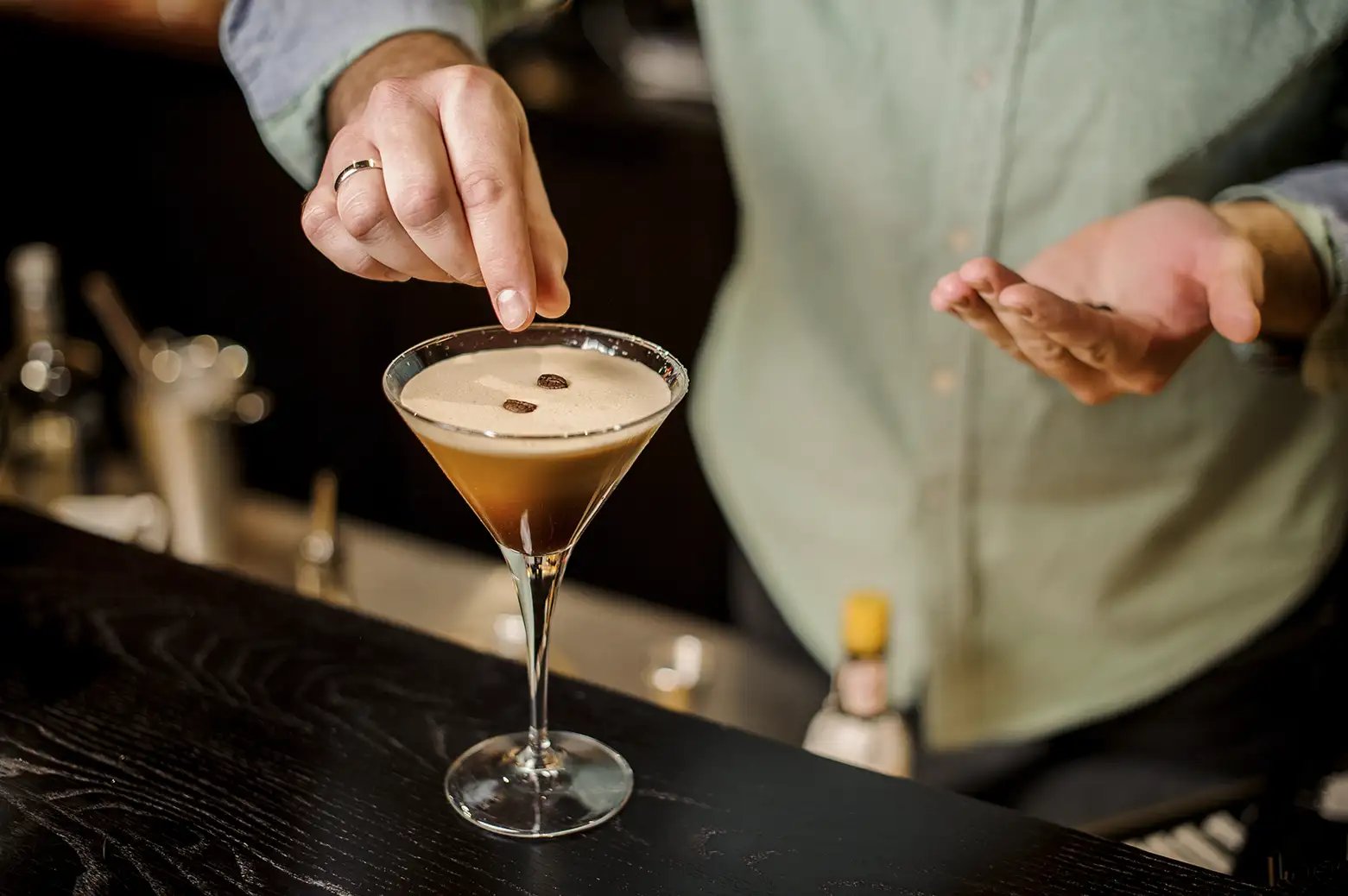 Bartender placing espresso coffee beans on top of an espresso martini as a garnish