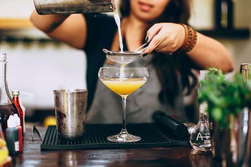 A bartender pouring a mixed drink cocktail through a strainer