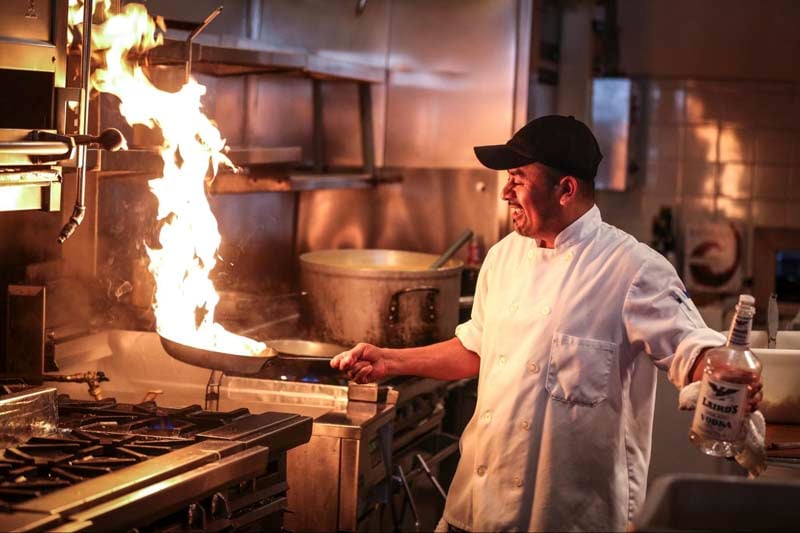 Chef cooking in kitchen while flipping food in a pan over a flame