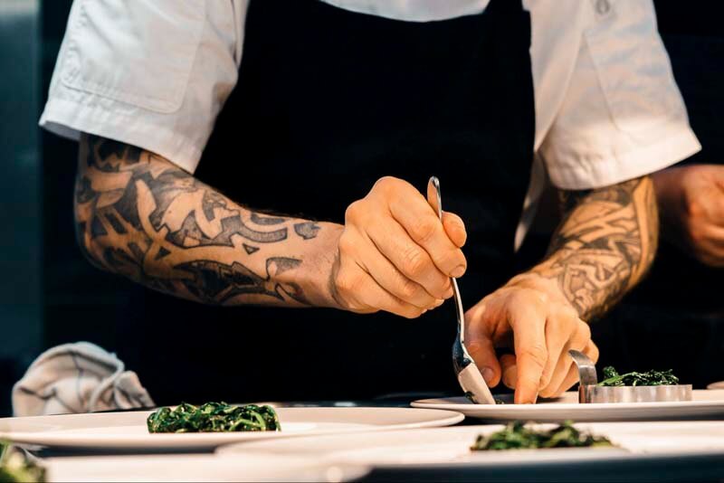 close-up-of-tattooed-arm-chef-plating-various-dinner-plates