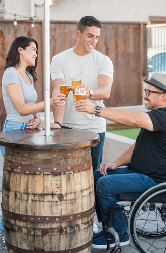 Young couple shares a beer with friend in wheelchar at outdoor bar