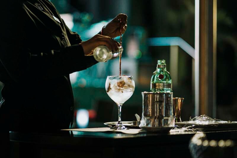 An photo of a bartender pouring and stirring a drink in a darkly lit bar atmosphere