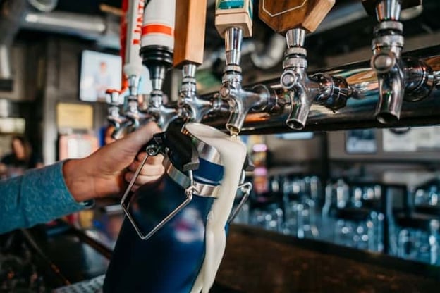 Up close image of bartender filling a growler at a beer tap wall