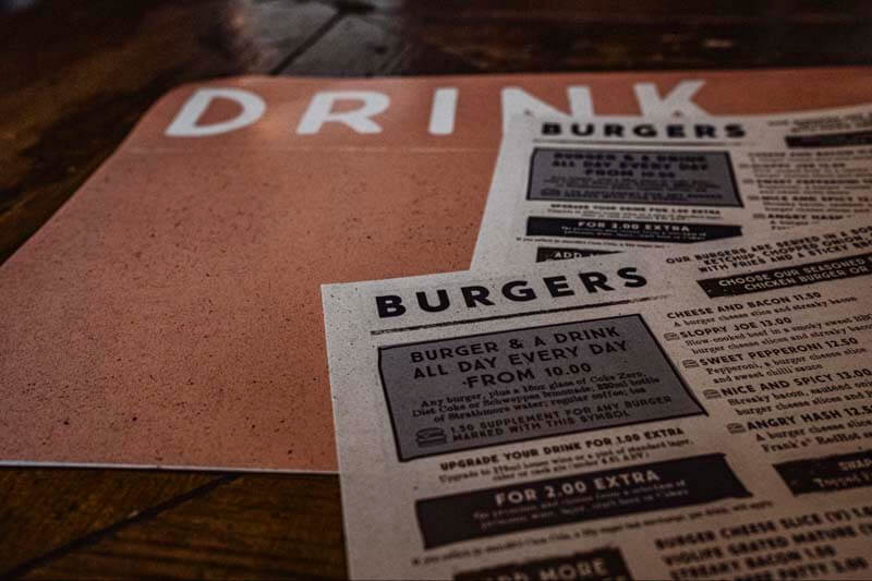 Food and drink menus sitting on a table featuing burgers