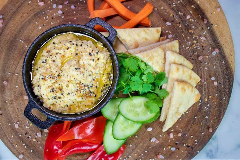 Fresh hummus served with warm pita chips and a vegetable variety at a bar as a shareable starter