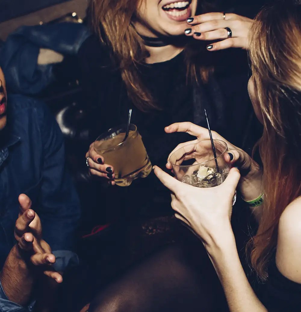 A group of people enjoying whiskey cocktails at bar or nightclub setting - up close photo