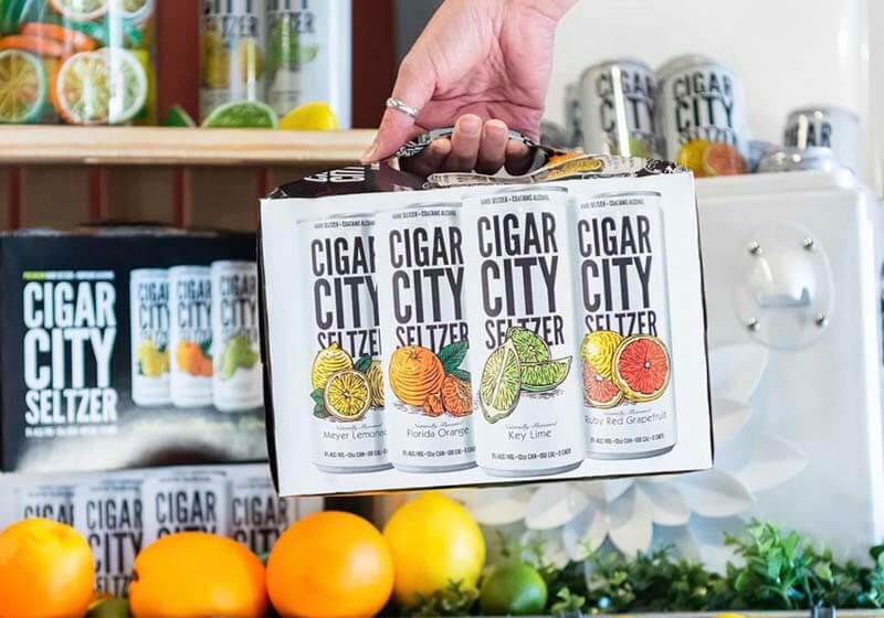 Photo of a hand holding a case of a Cigar City Seltzer variety pack