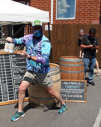 Man showcasing craft beer six pack at curbside pickup at Divine Barrel Brewing Company