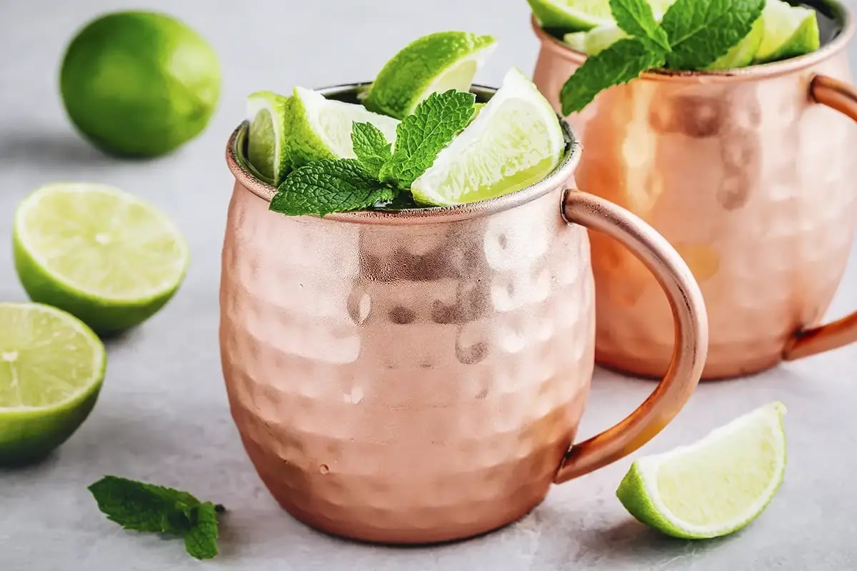 A Mexican Mule tequila cocktail served in a traditional bronze mule mug with lime garnishes