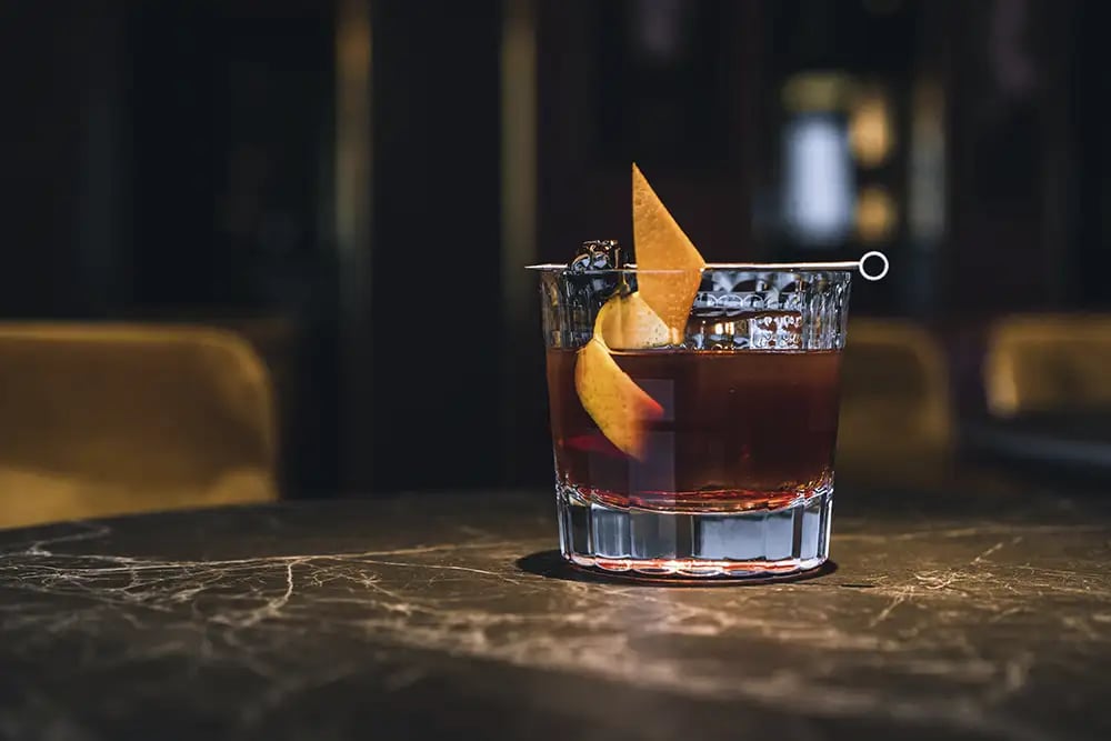 An Old Fashioned whiskey cocktail with an orange peel garnish at a bar