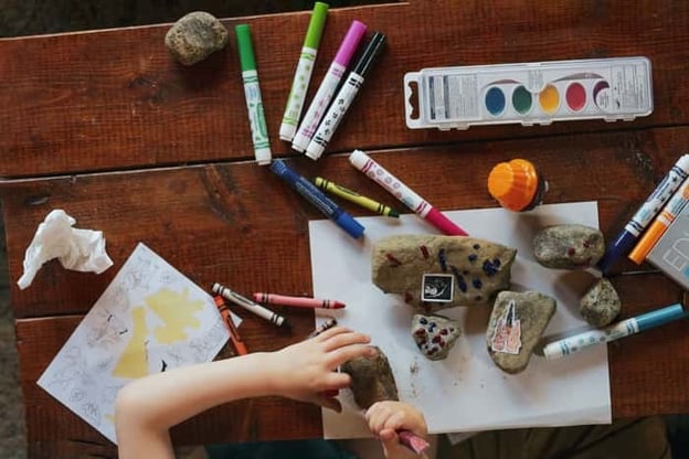 Overhead shot of child coloring rocks with paint and markers