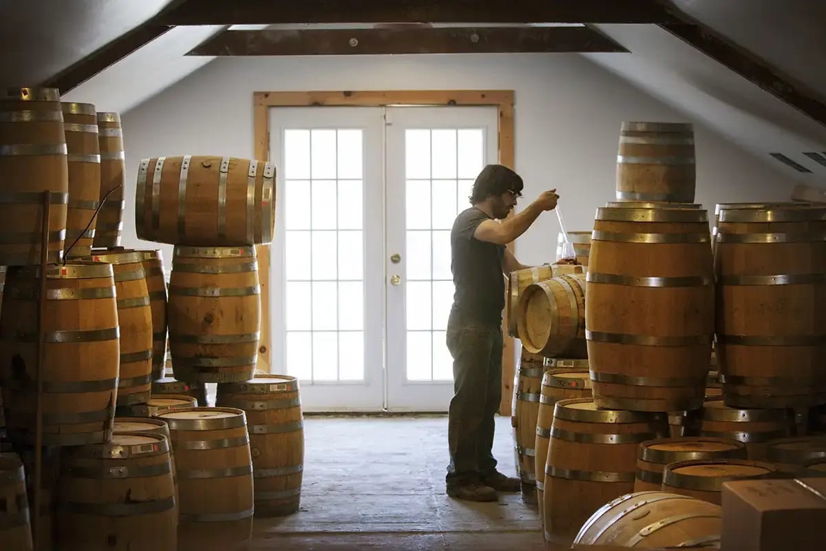 A persons tests a small sample of whiskey from a barrel