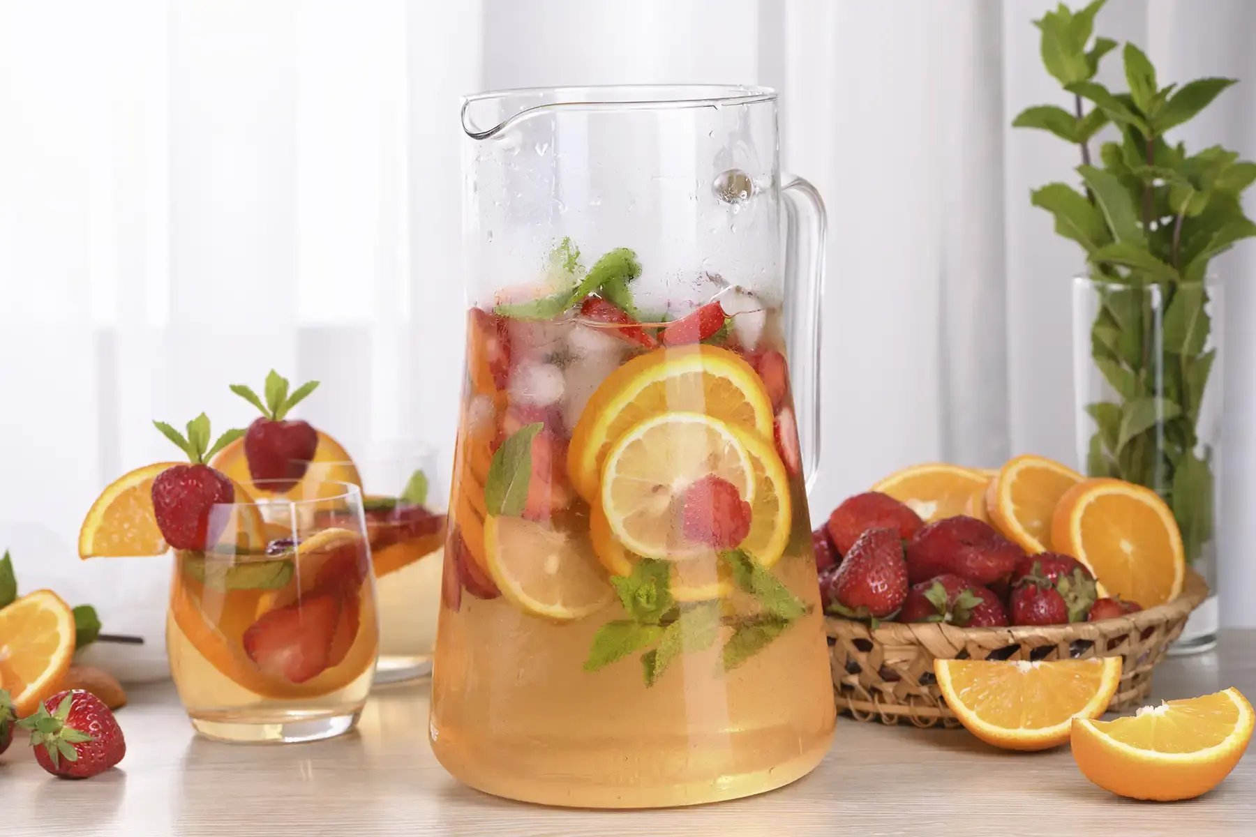 A pitcher of sangria made with oranges, strawberries, and mint leaves