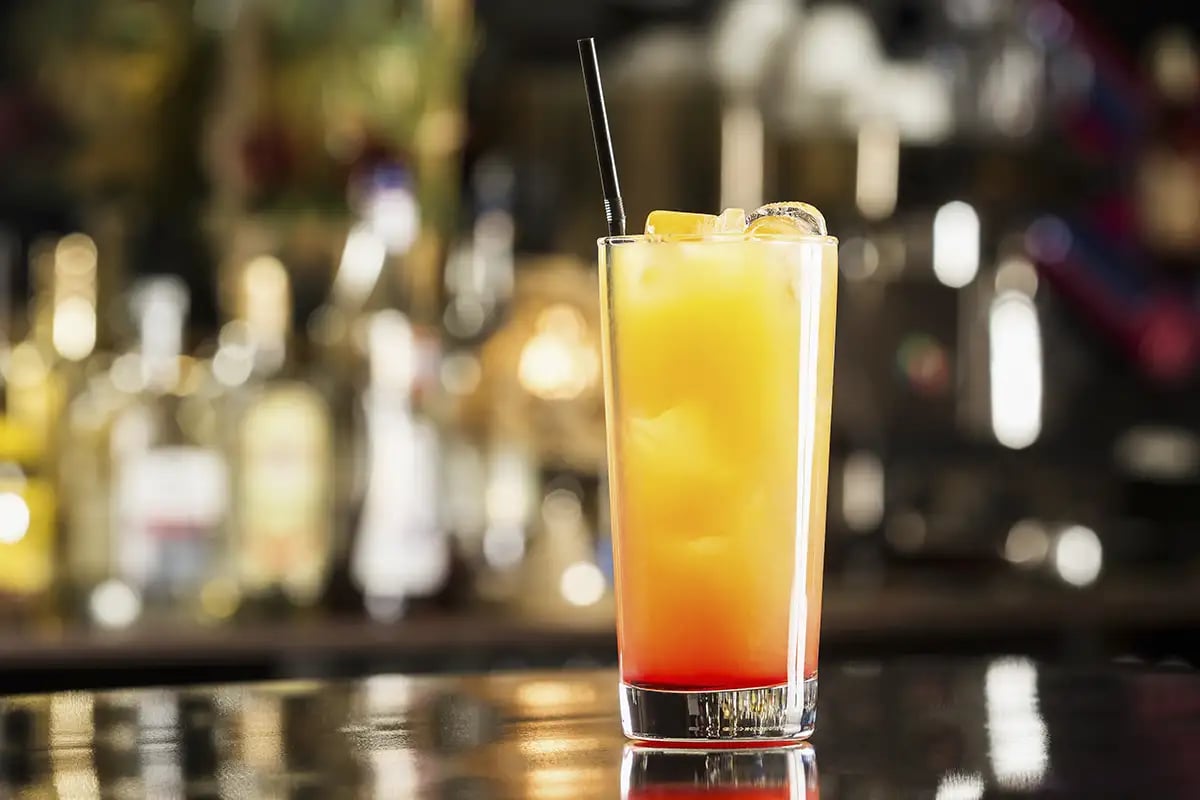 A Tequila Sunrise cocktail served in a tall glass sitting on a dark bar