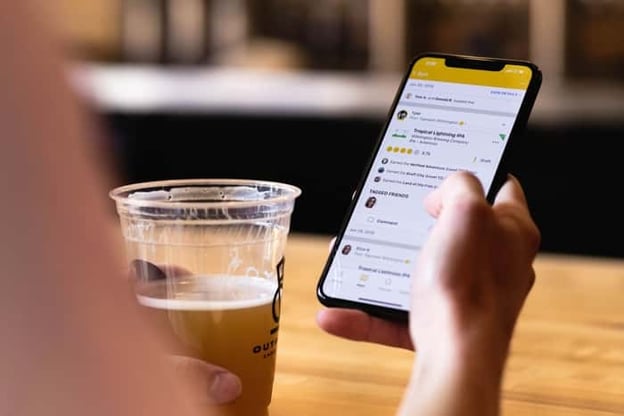 Untappd user scrolling through app at table with beer