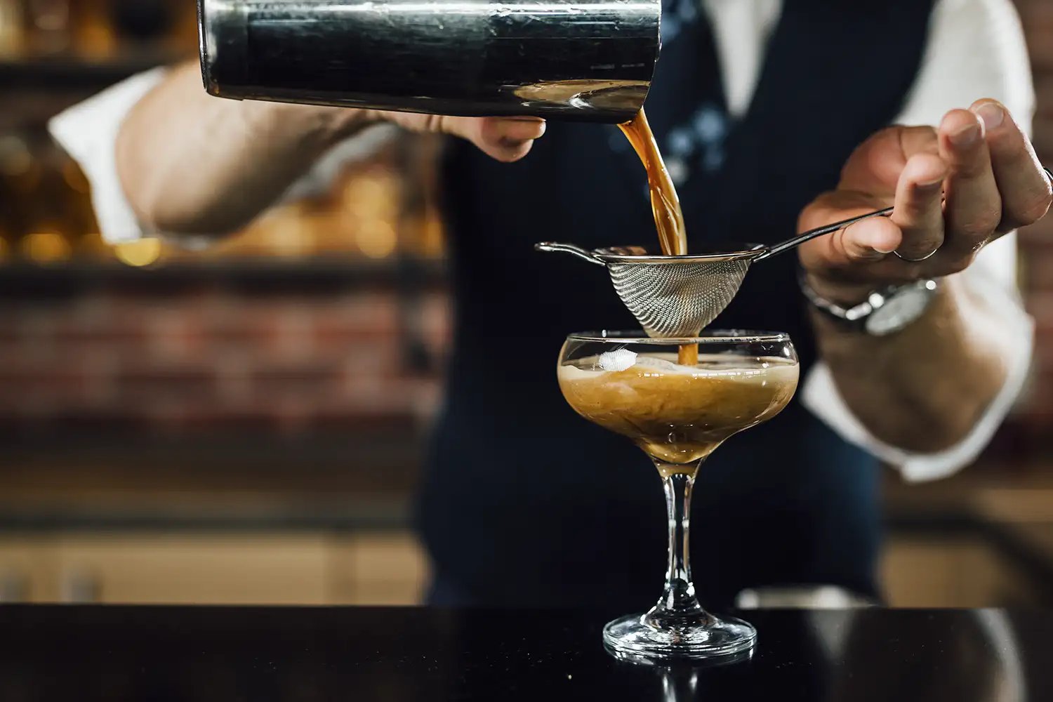 Up close photo of a bartender pouring and straining an espresso martini into a glass