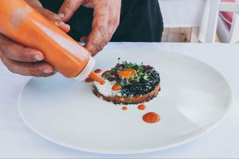 Up close image of a chef finishing a plate with a sauce drizzles and dots