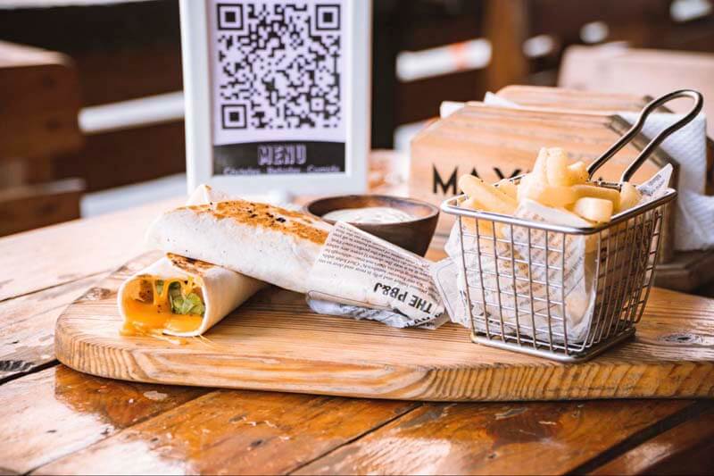 A wrap sandwich and fries on a platter with a QR code table card in the background