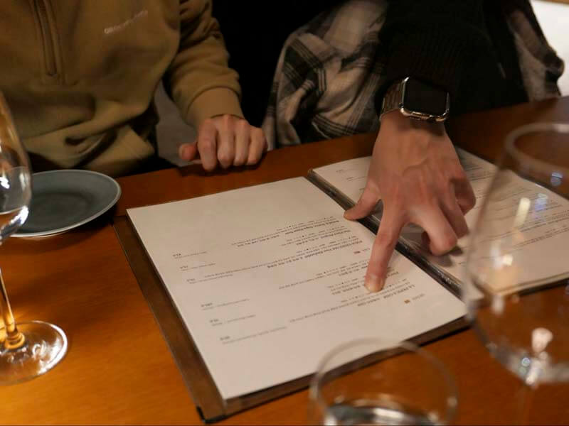Close up photo of a waiter's hand pointing at and explaining a prix fixe menu to a restaurant guest