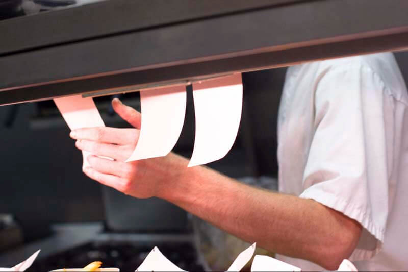 A chef or line cook taking a food delivery order ticket in a busy kitchen or restaurant