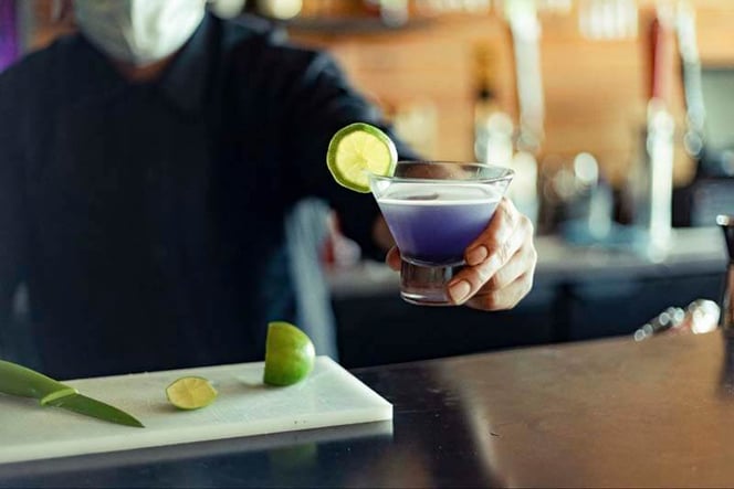 Up close shot of bartender serving a mixed cocktail with a lime garnish