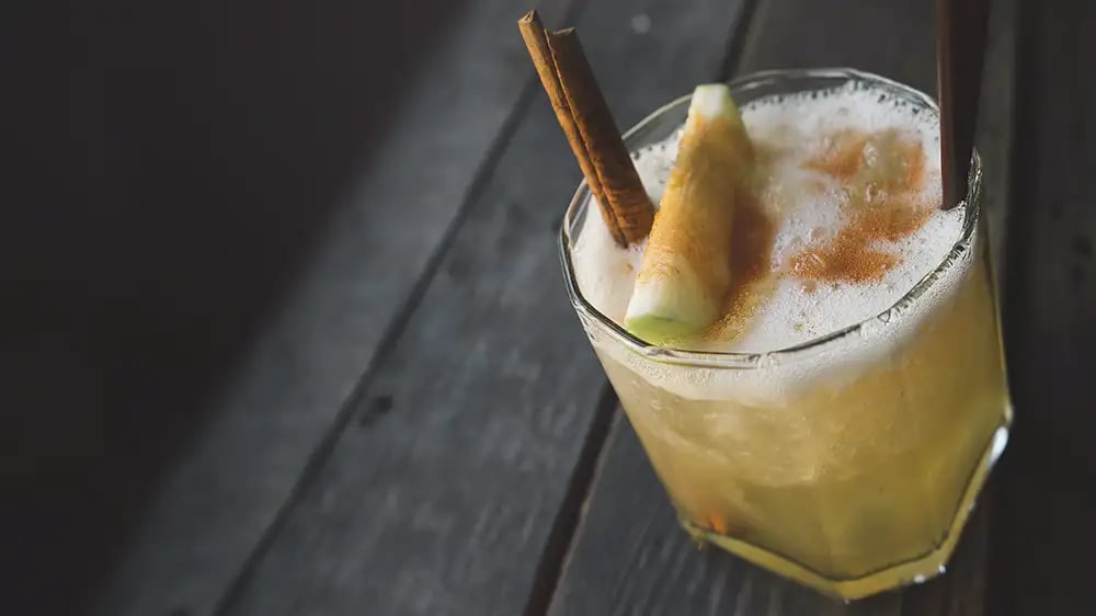 A whiskey cocktail with apple and cinnamon garnish on a wooden table
