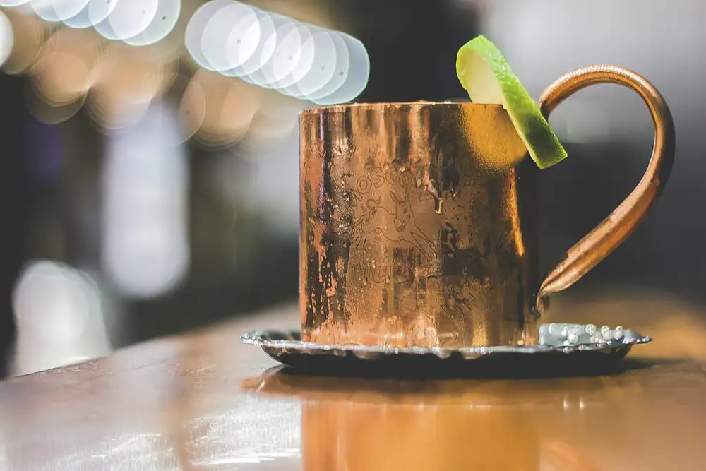 A whiskey cocktail served in a bronze mule style container with a lime wedge garnish